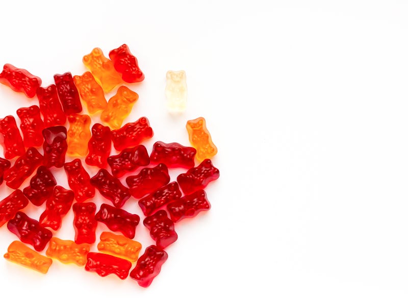 A bunch of bright red and orange jelly bears are displayed on a white background, creating contrast ...