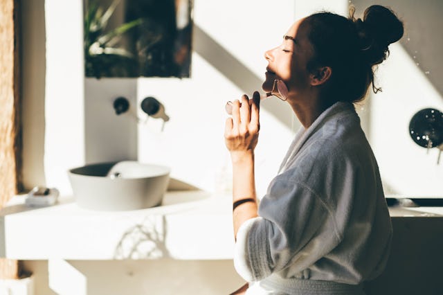 Woman doing face massage with a roller at the bathroom.