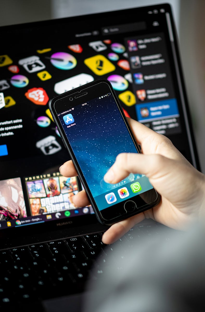 ILLUSTRATION - 02 May 2021, Berlin: A woman holds an IPhone with the app store in front of a screen ...