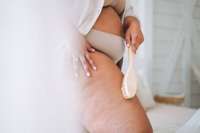 Crop photo of young plus size woman in underwear doing body massage with dry wooden brush in bedroom...