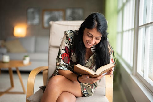 Women wellness. Portrait of smiling beautiful young multiracial woman reading a book in a rocking ch...