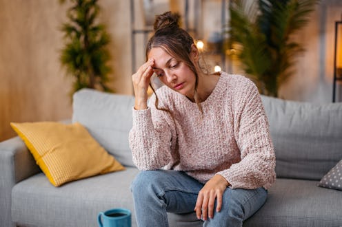 Mid-adult woman having a headache while sitting on the sofa at home.