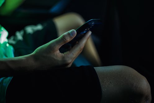 A hand scrolls through a smartphone, bathed in an ethereal green light. The image evokes a sense of ...
