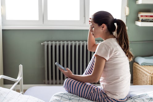Young woman in pajamas, sitting on the bed in the morning and scrolling on the phone