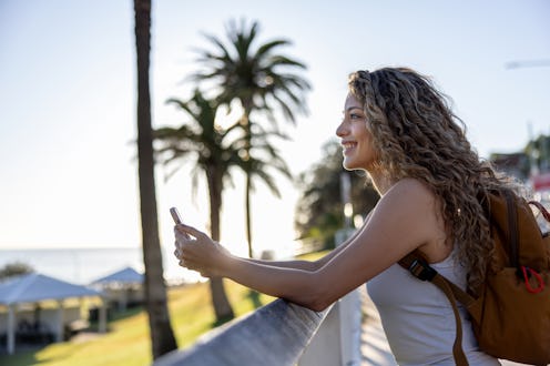 Profile view of a happy woman smiling outdoors while using her cell phone - lifestyle concepts