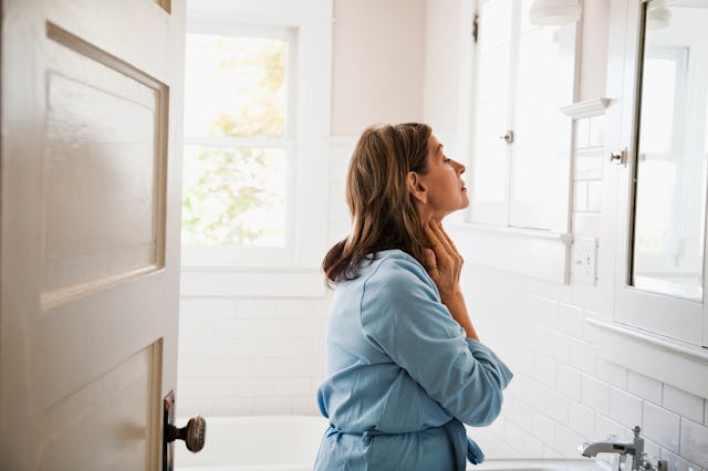 Woman examines her neck in the bathroom mirror, in a story about getting skin tags as you age.