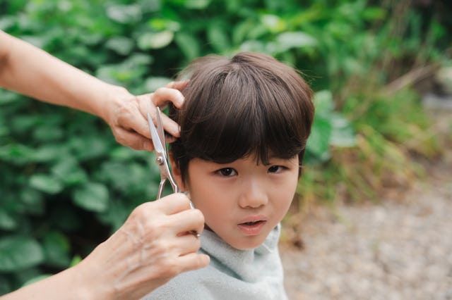A grandmother cuts her grandchild's hair outside.