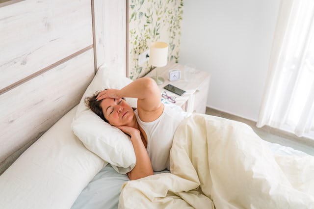 Woman in bed touching her head having a headache. High resolution 42Mp studio digital capture taken ...