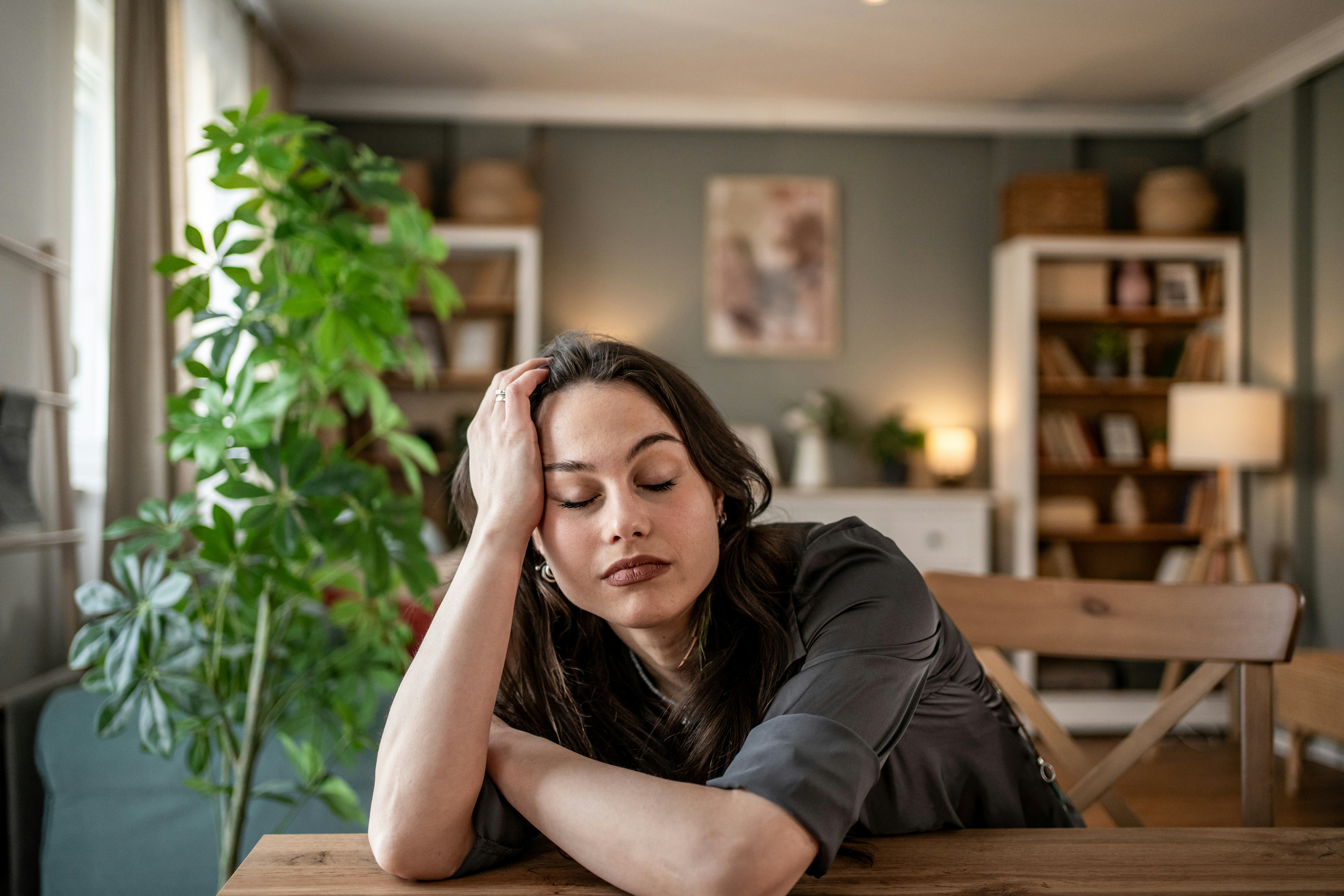 Young woman resting her head on a table, eyes closed and exuding a sense of tiredness and stress whi...