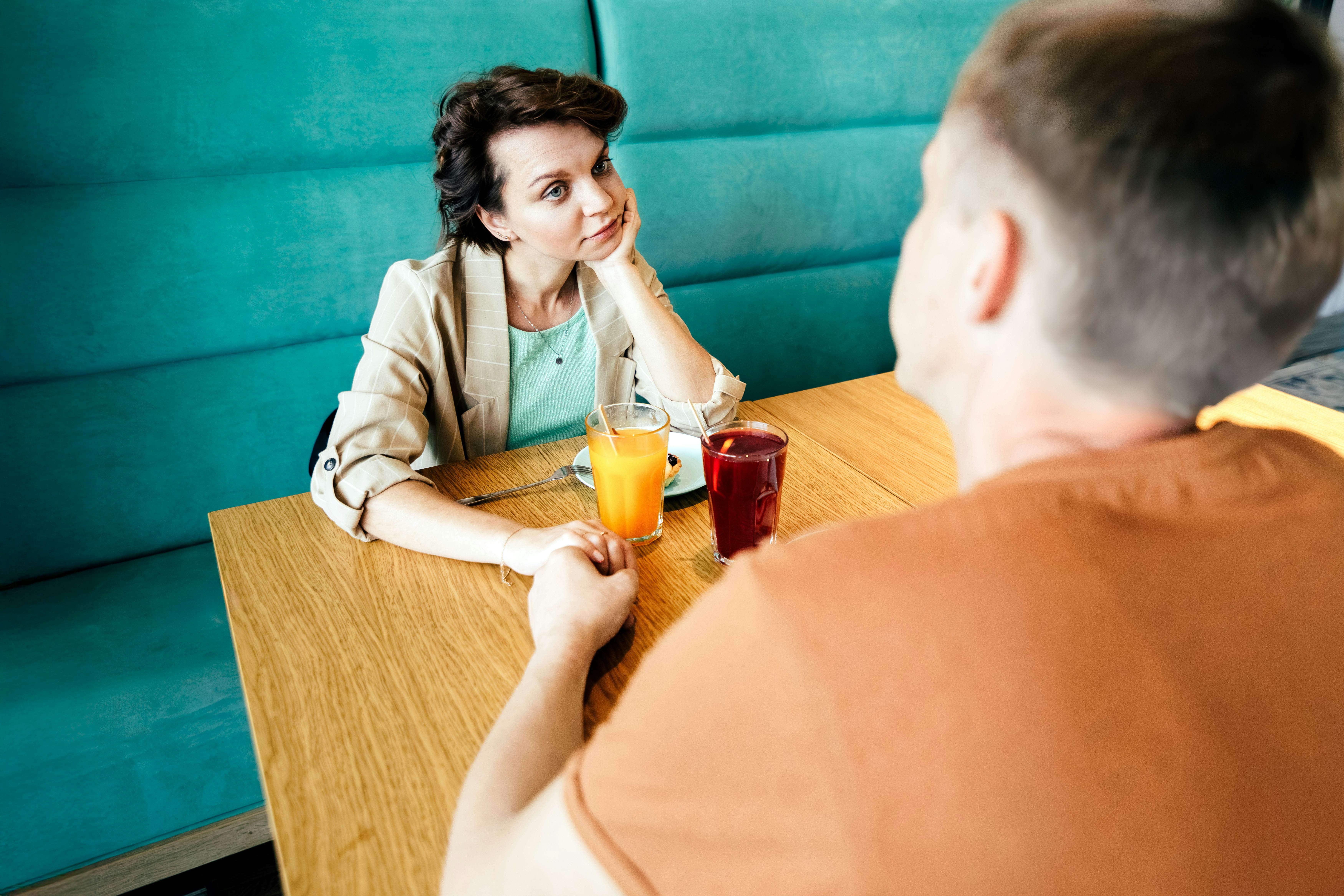 Bored woman looking away while holding hands with man at restaurant having relationship problems