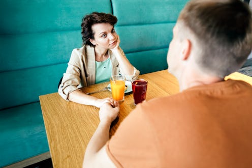 Bored woman looking away while holding hands with man at restaurant having relationship problems