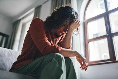 A concerned woman leans on her arm, sitting in a thoughtfully lit modern interior. The sunlight thro...