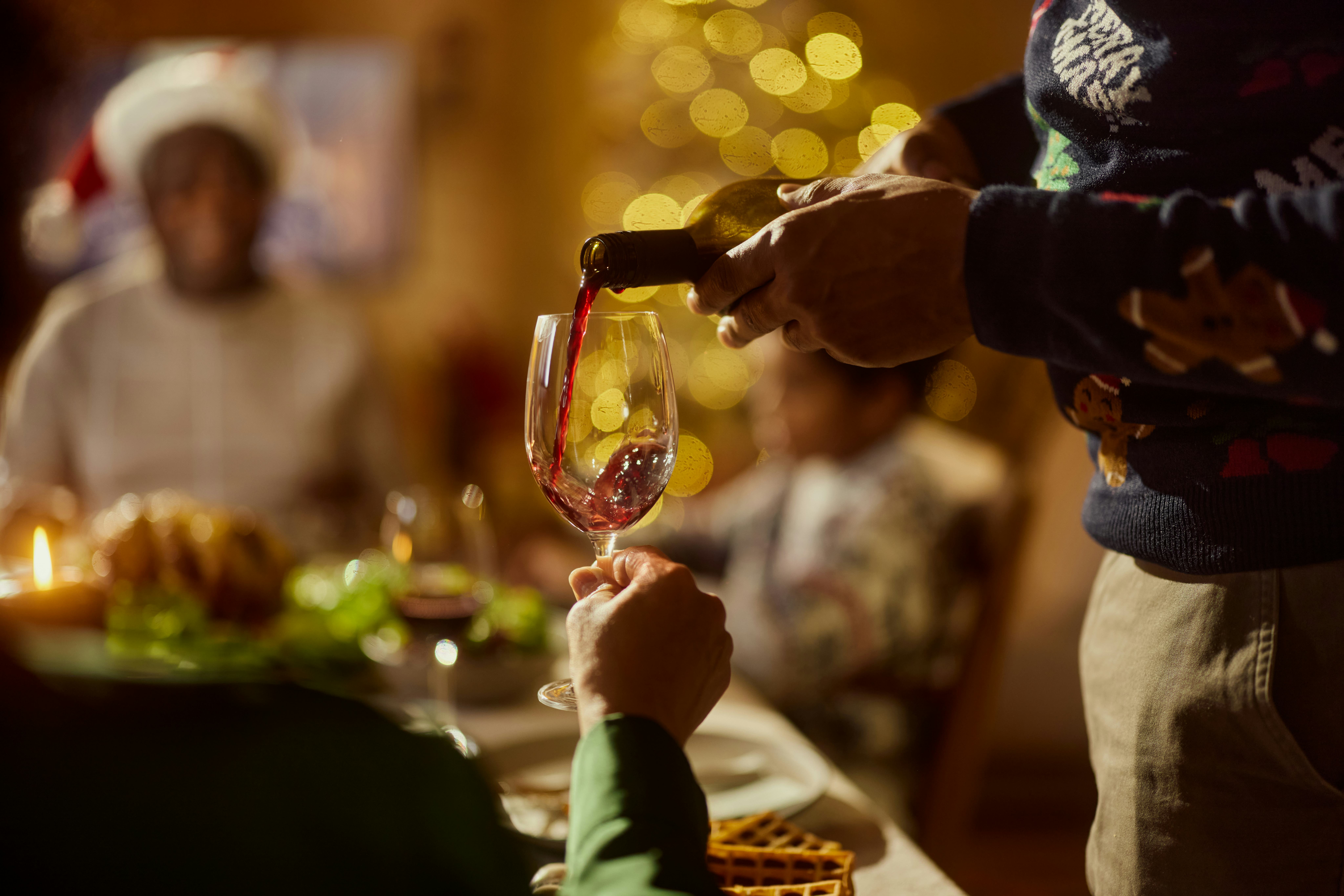 Close up of unrecognizable African American man pouring red wine into woman's glass during a meal on...