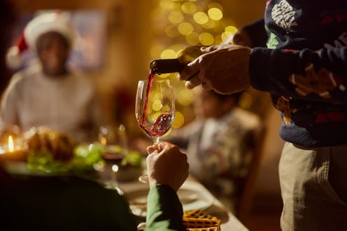 Close up of unrecognizable African American man pouring red wine into woman's glass during a meal on...