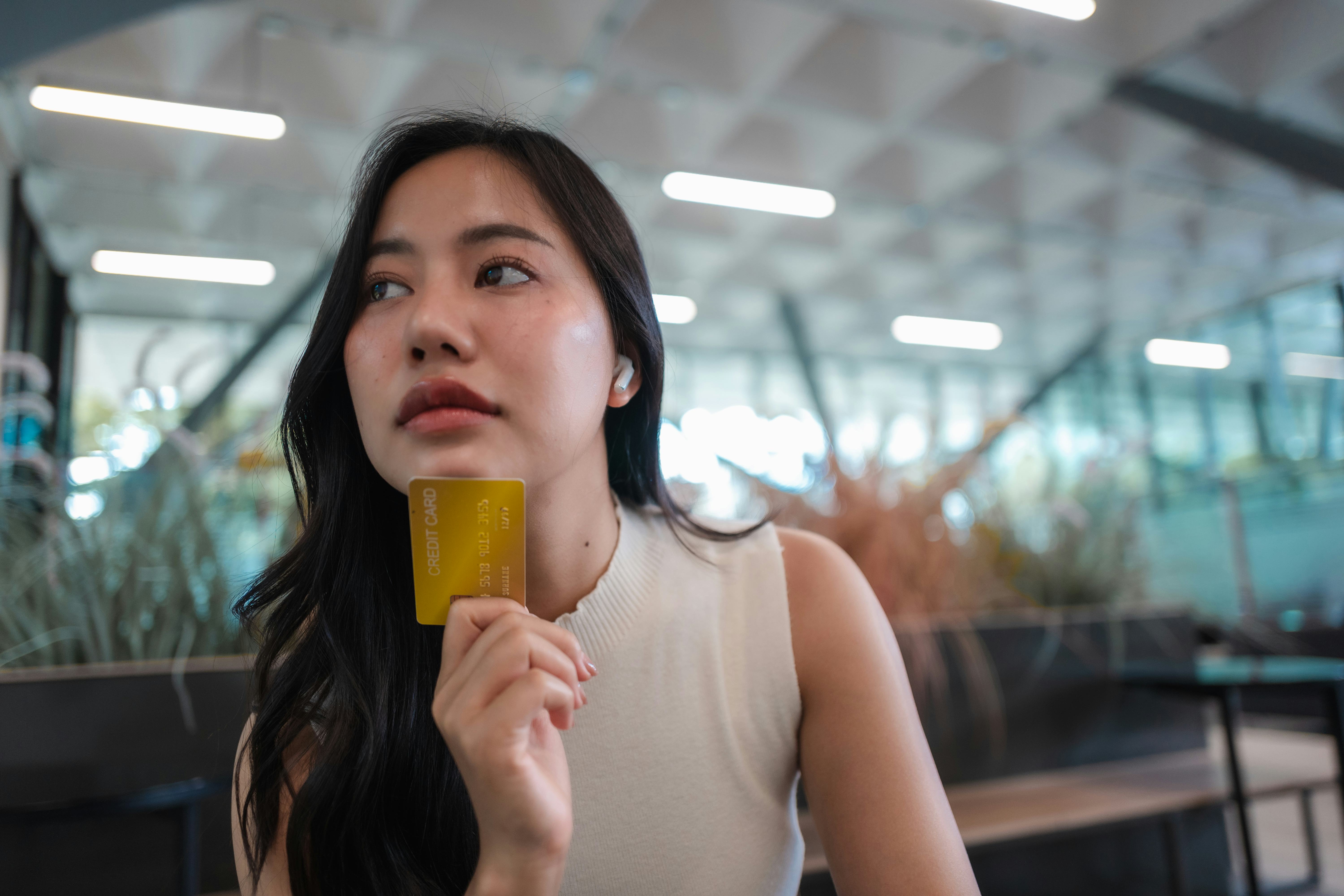 Thoughtful young woman holding credit card and thinking about shopping, e-commerce and online bankin...