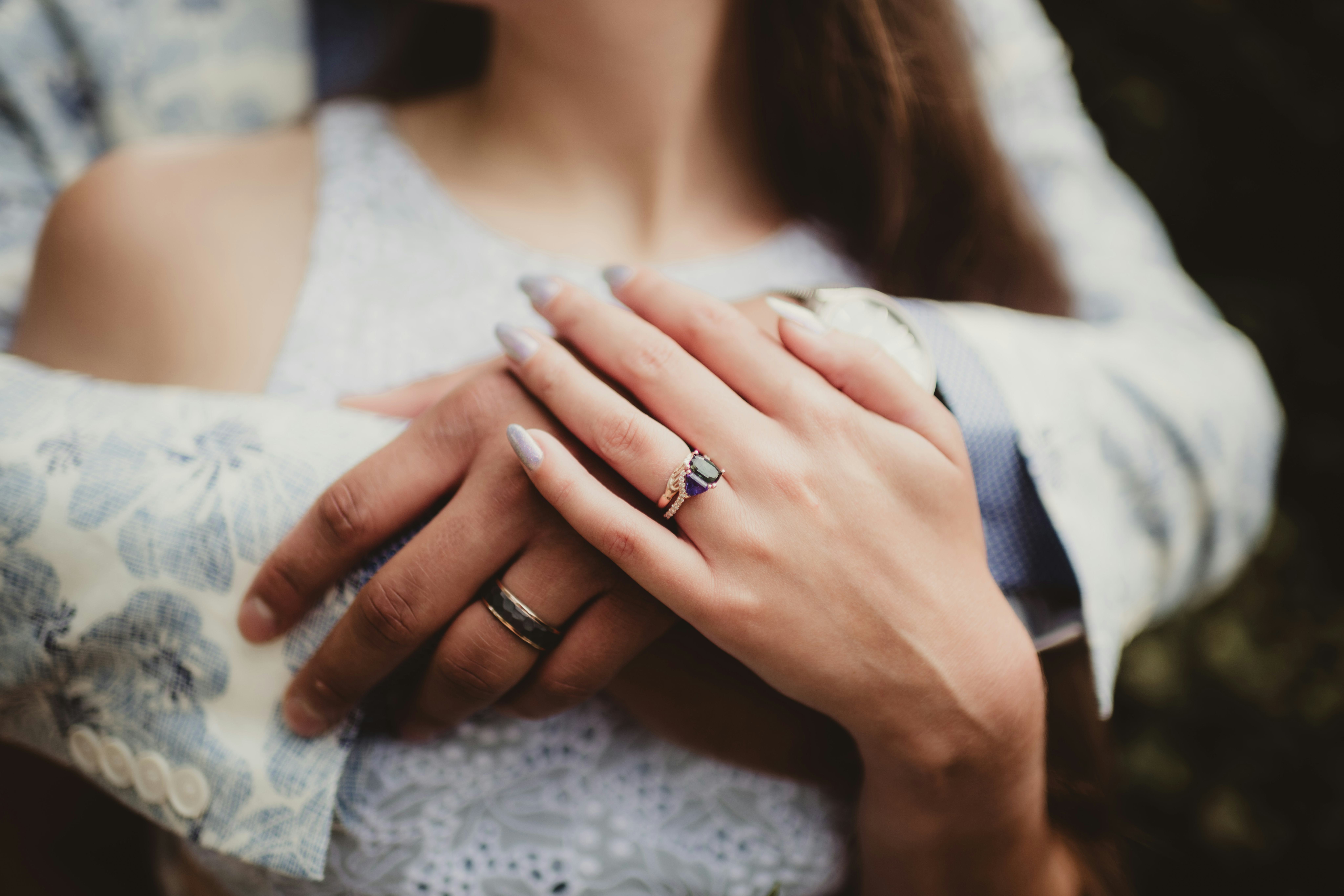 Man embracing woman with focus on wedding rings and sapphire engagement ring