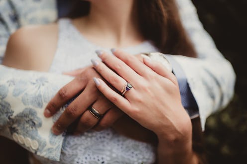 Man embracing woman with focus on wedding rings and sapphire engagement ring
