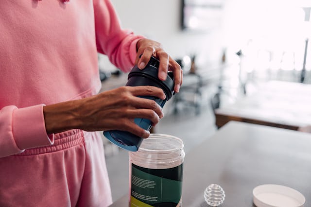 Woman preparing protein shake at home before leaving to the gym.