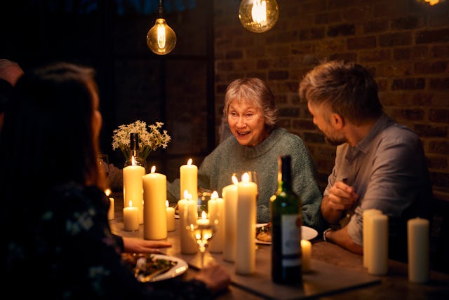 Mixed age group of people enjoying candlelit evening meal, sitting around dining table, woman in her...