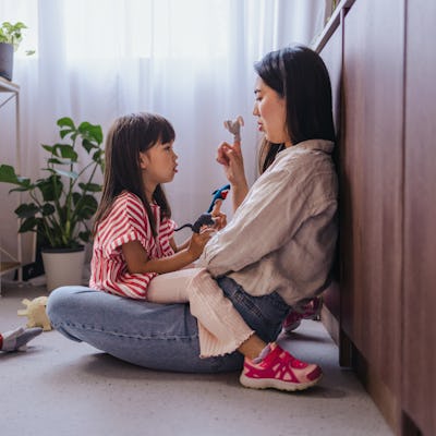 A side view of a smiling Japanese female having fun with her adorable playful daughter while sitting on the floor.