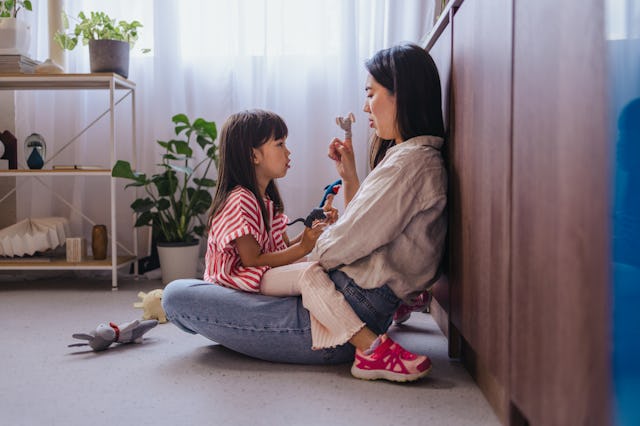 A side view of a smiling Japanese female having fun with her adorable playful daughter while sitting...