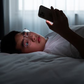 Teenager boy lying in bed using mobile phone