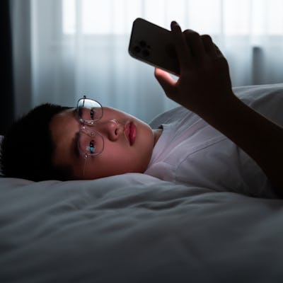 Teenager boy lying in bed using mobile phone