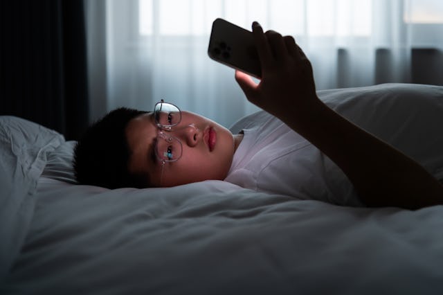 Teenager boy lying in bed using mobile phone