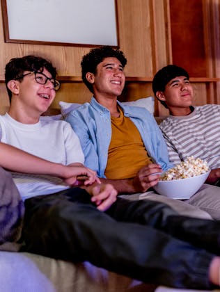 Teenage boys talking and eating popcorn while watching movie at home.