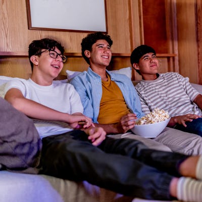Teenage boys talking and eating popcorn while watching movie at home.