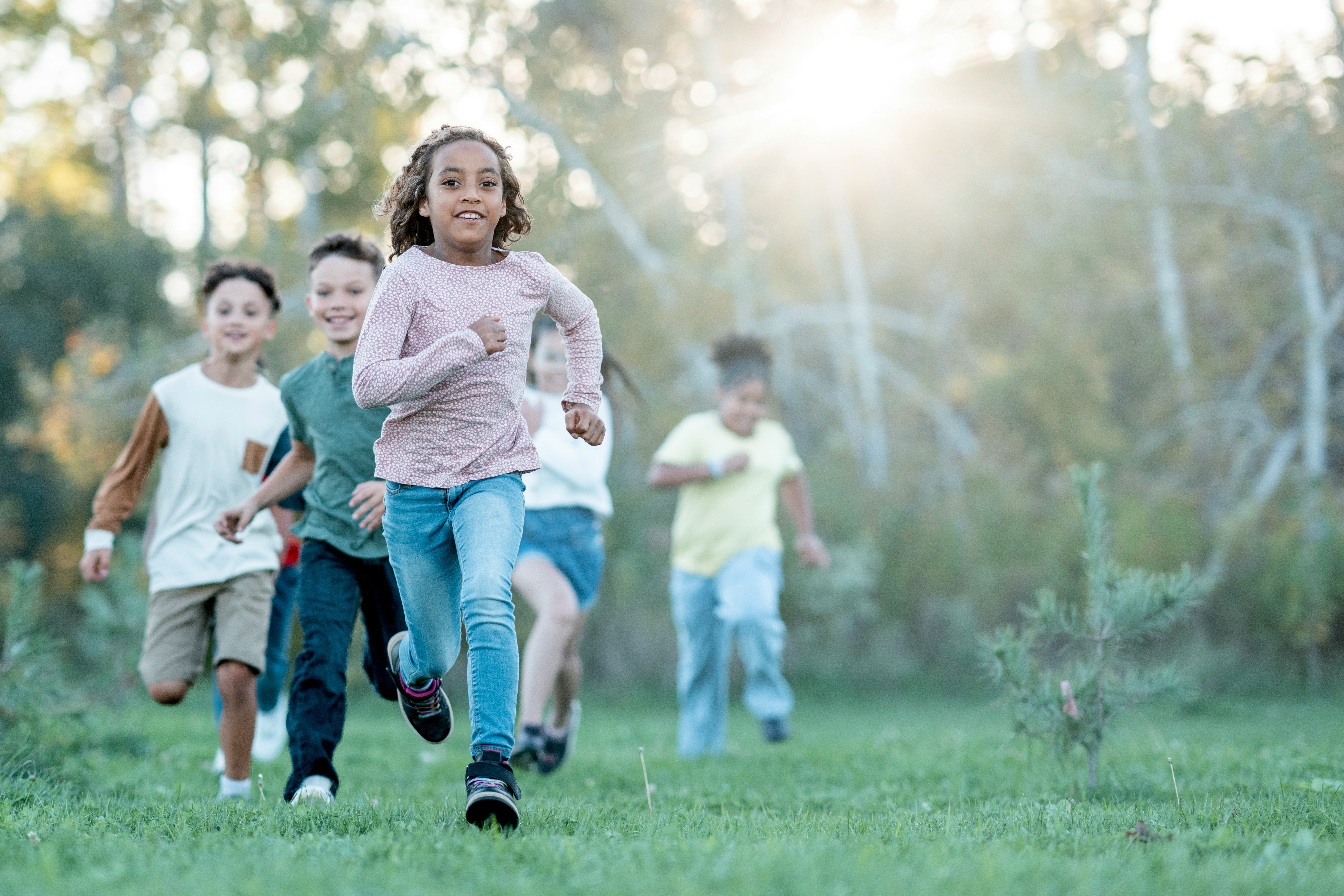 A joyful, diverse group of children runs together in a sunlit park, capturing energy, friendship, an...