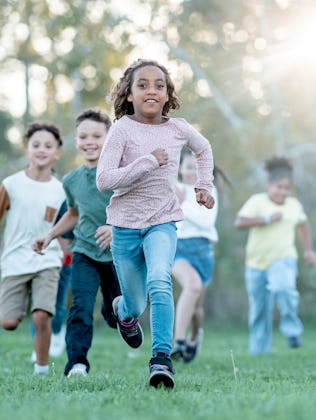 A joyful, diverse group of children runs together in a sunlit park, capturing energy, friendship, an...