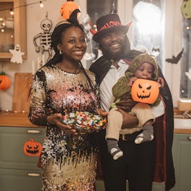 Portrait of parents with child wearing Halloween costumes and having party at home.