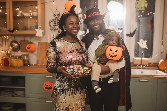 Portrait of parents with child wearing Halloween costumes and having party at home.