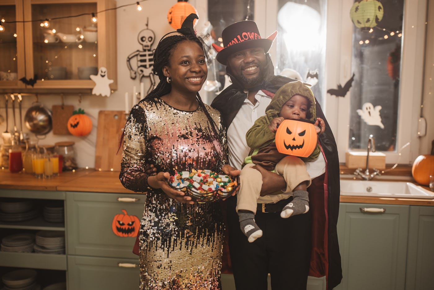 Portrait of parents with child wearing Halloween costumes and having party at home.