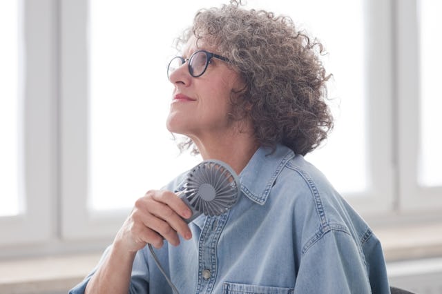 Menopausal mature woman wearing denim shirt and eyeglasses sitting in the modern office, having a ho...