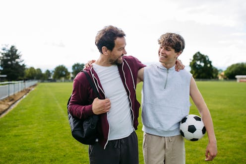Father and teenage son playing football on a field at sunset.