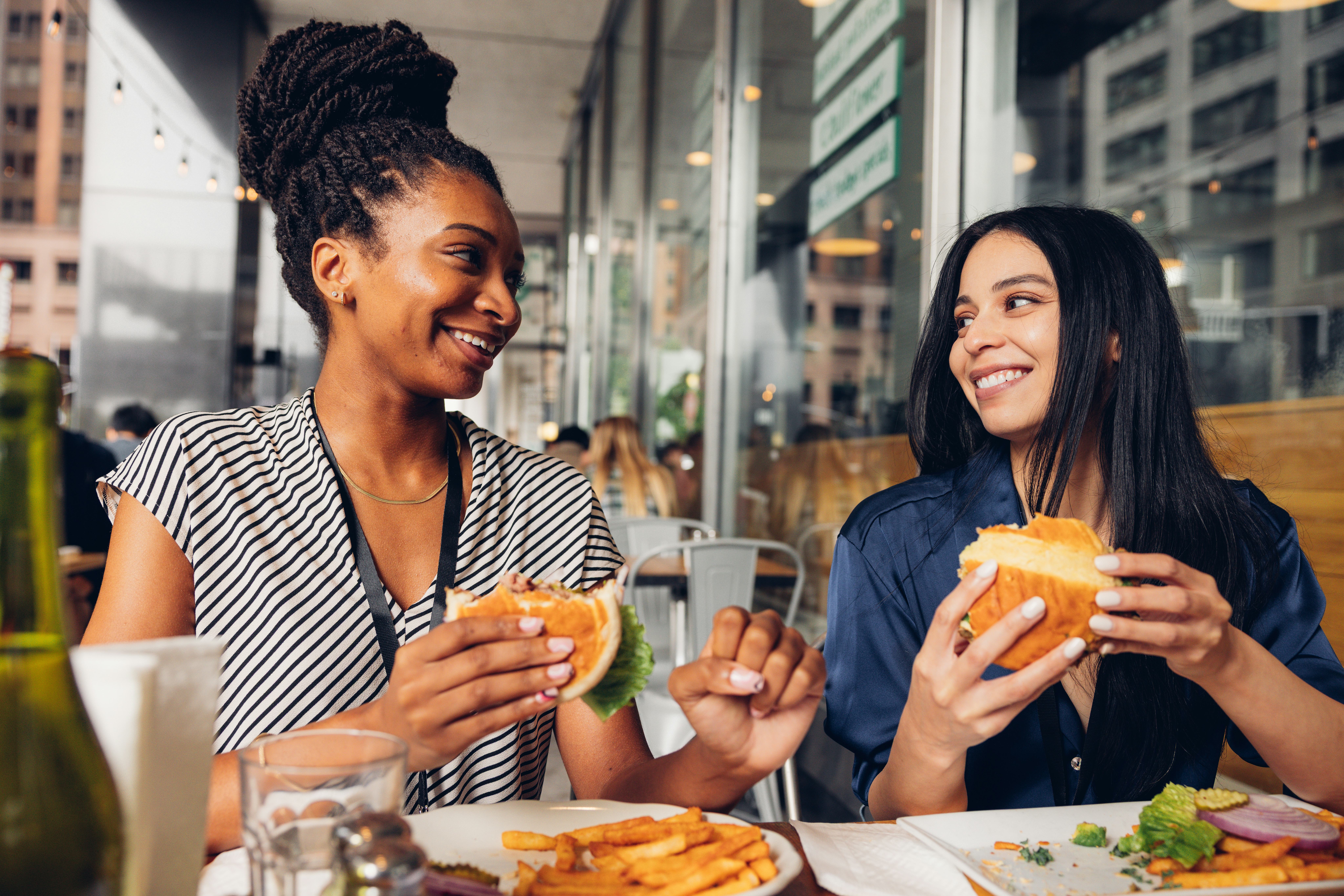 Two colleagues sitting in a outdoor table eating at lunch break.