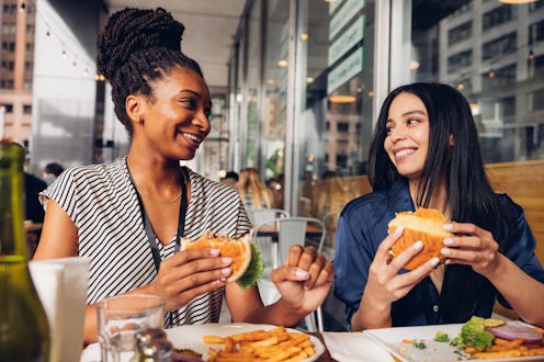 Two colleagues sitting in a outdoor table eating at lunch break.