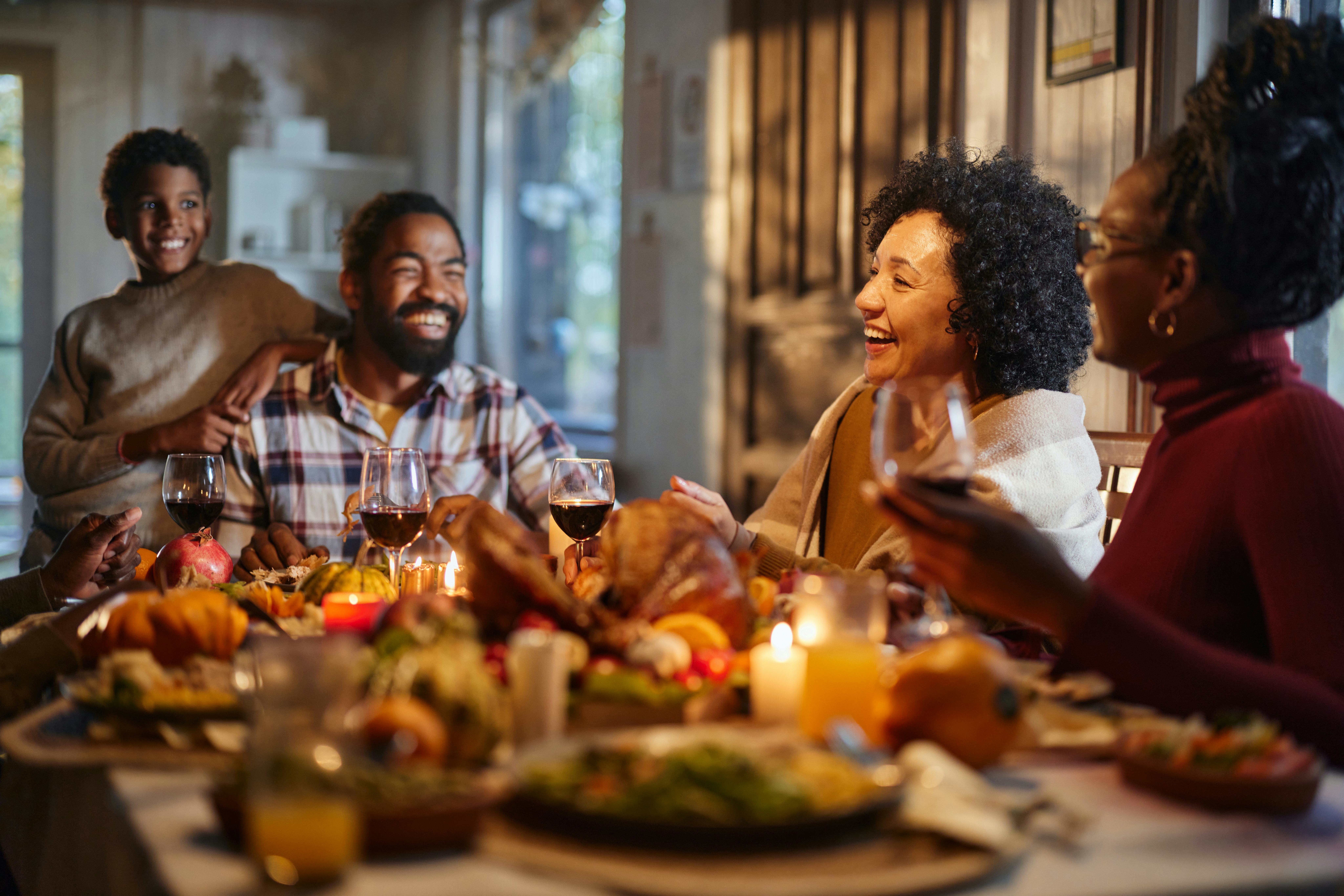 Happy African American extended family talking during Thanksgiving meal at dining table. Focus is on...
