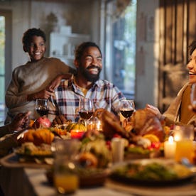 Happy African American extended family talking during Thanksgiving meal at dining table. Focus is on...