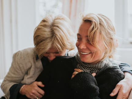 A mother hugs her adult daughter in a domestic living room. The scene is comfortable and loving as t...