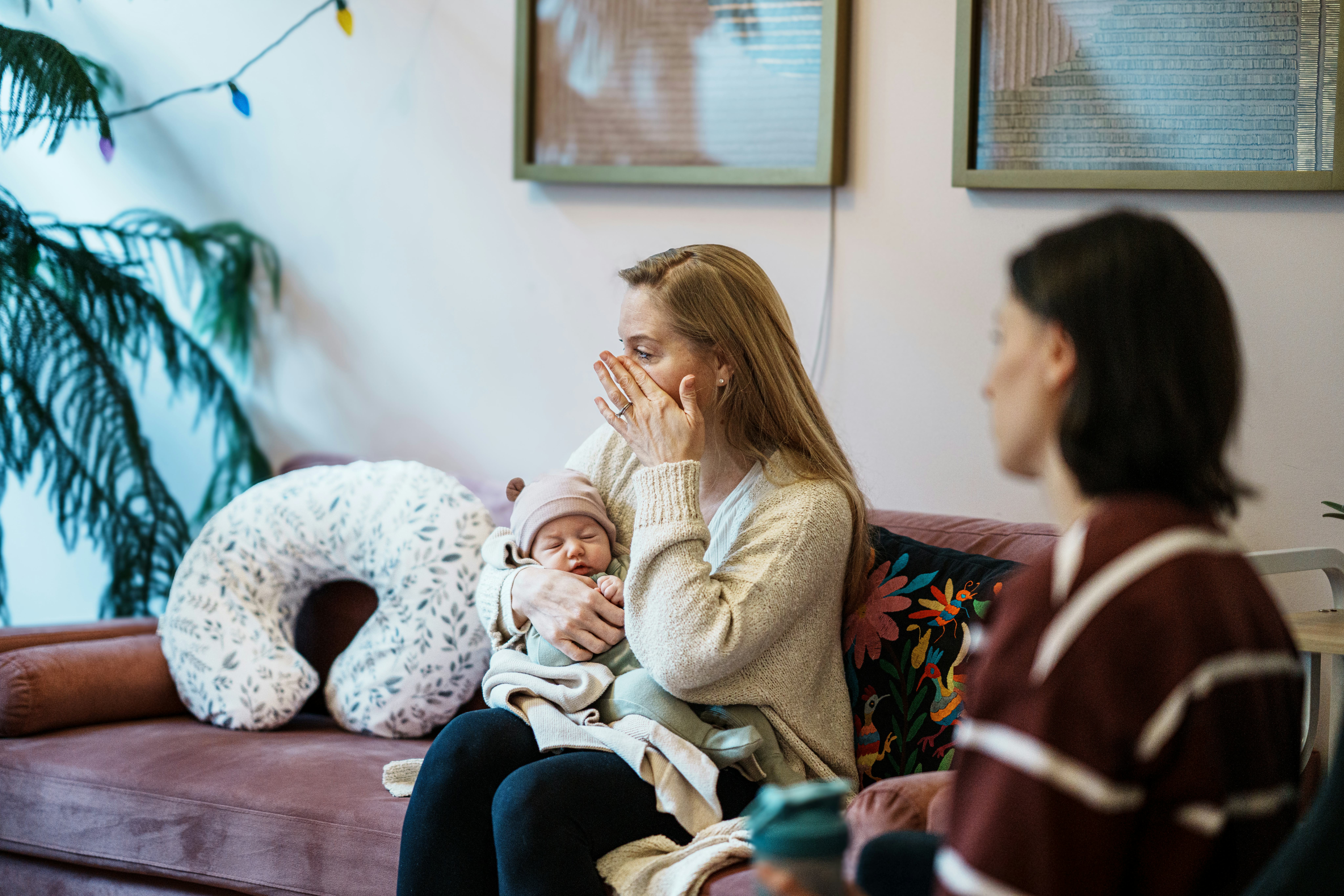 A woman holds her infant baby and wipes a tear from her cheek while talking with a other parents at ...