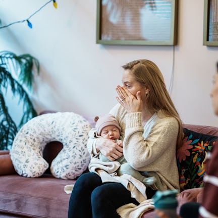 A woman holds her infant baby and wipes a tear from her cheek while talking with a other parents at ...
