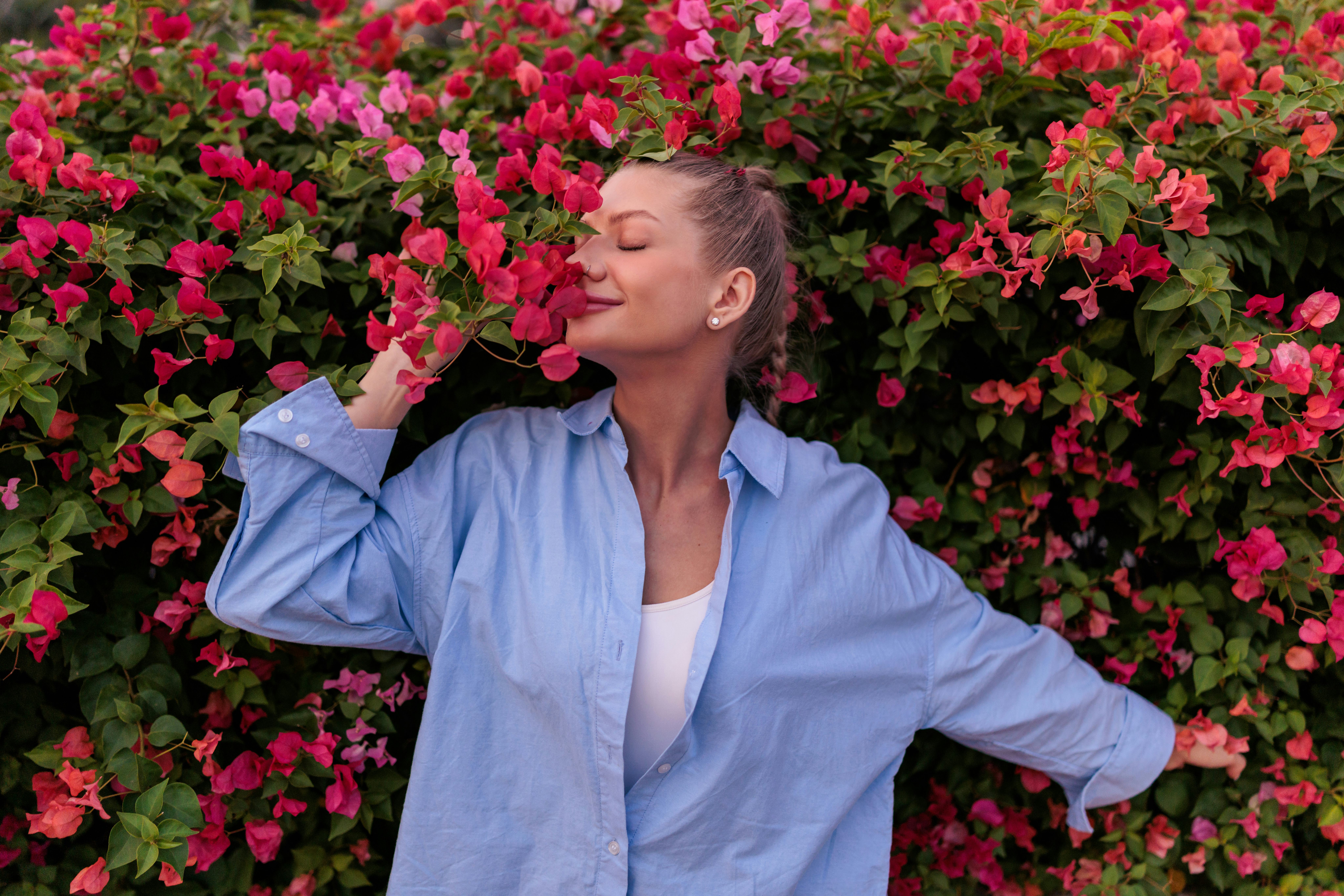 A serene white woman gently holds and inhales the delicate fragrance of pink flowers. With her eyes ...