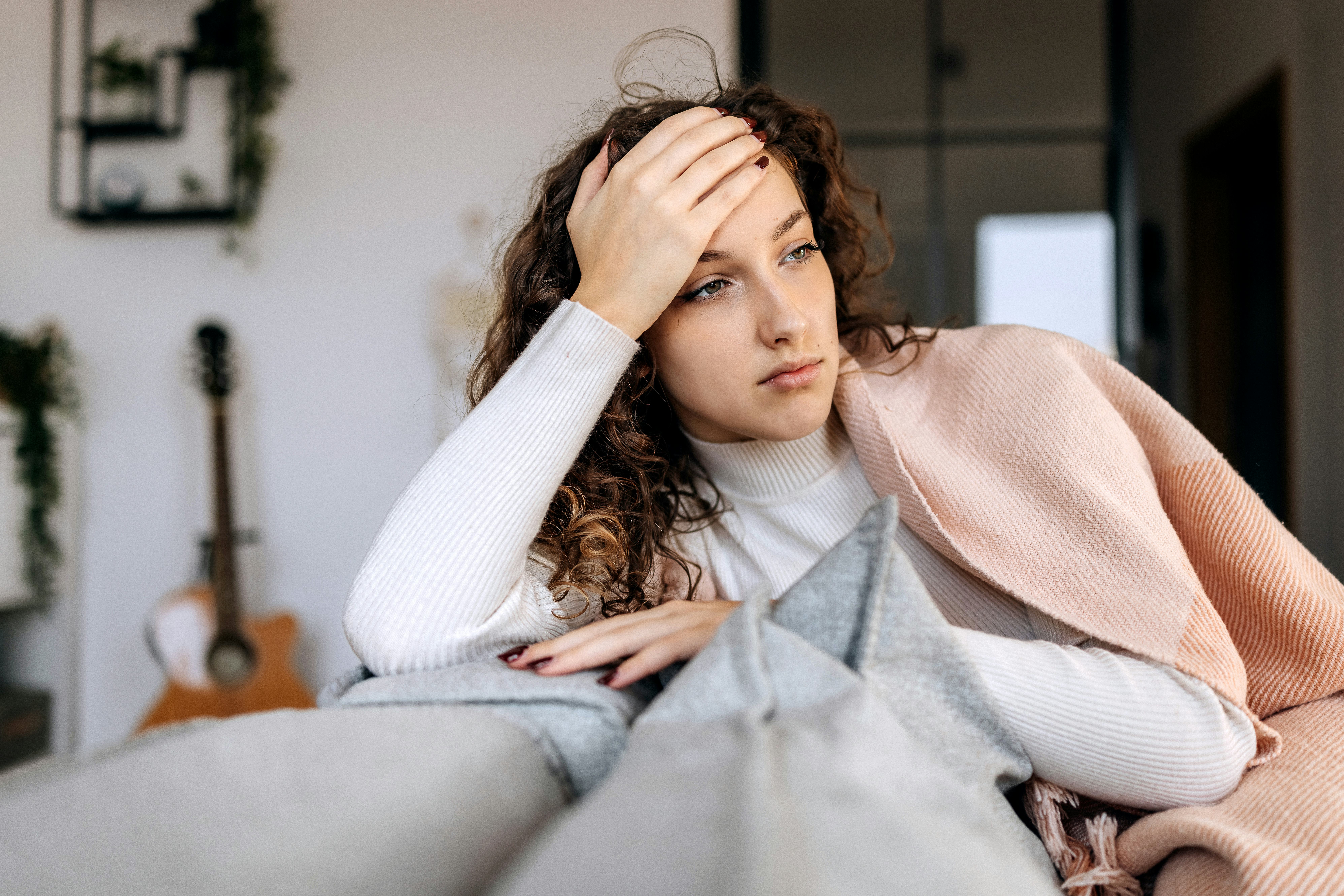 Tired young woman laying on a sofa wrapped in blanket