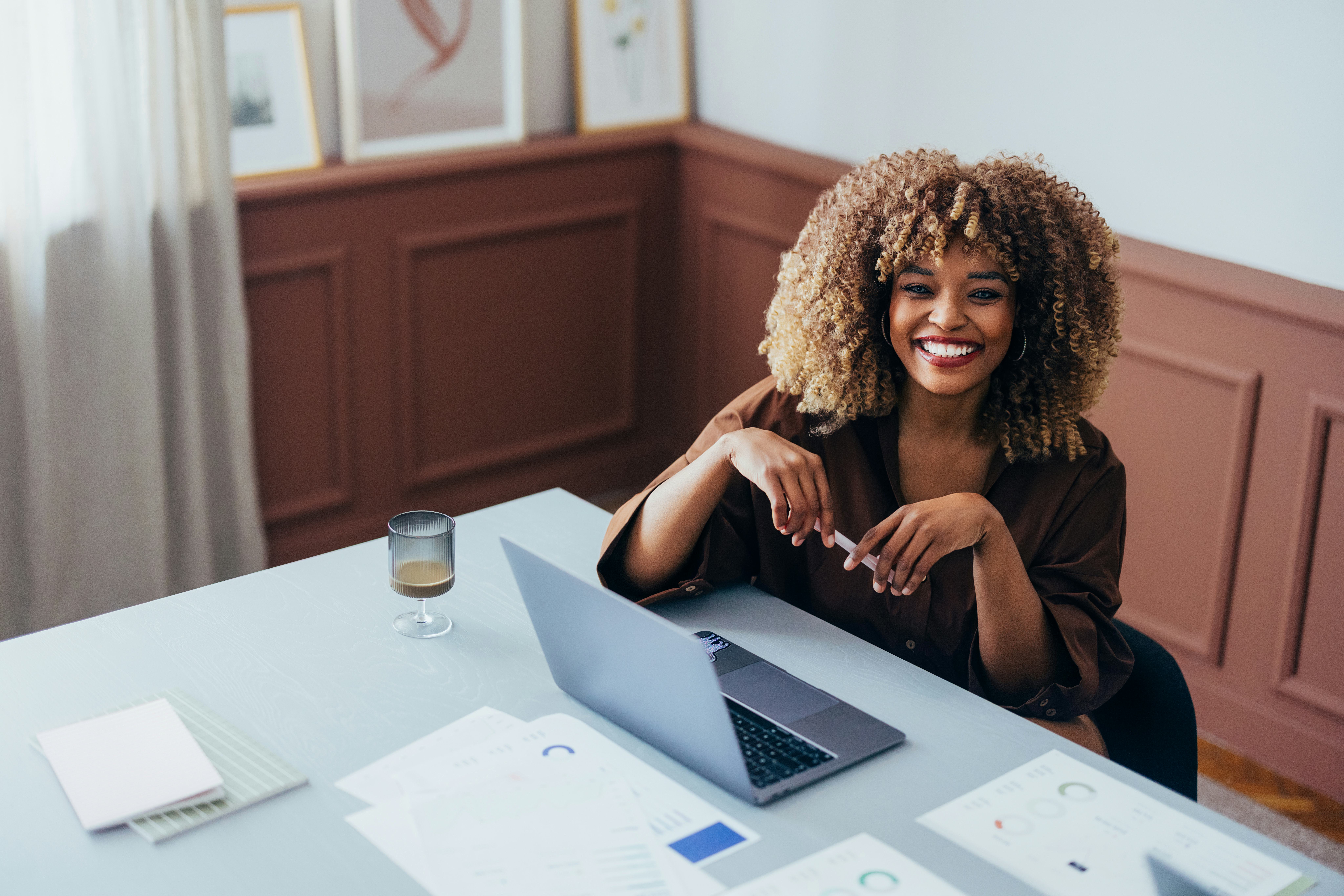 Professional workspace with a cheerful individual using a laptop, surrounded by documents and natura...