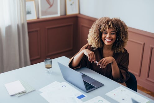 Professional workspace with a cheerful individual using a laptop, surrounded by documents and natura...