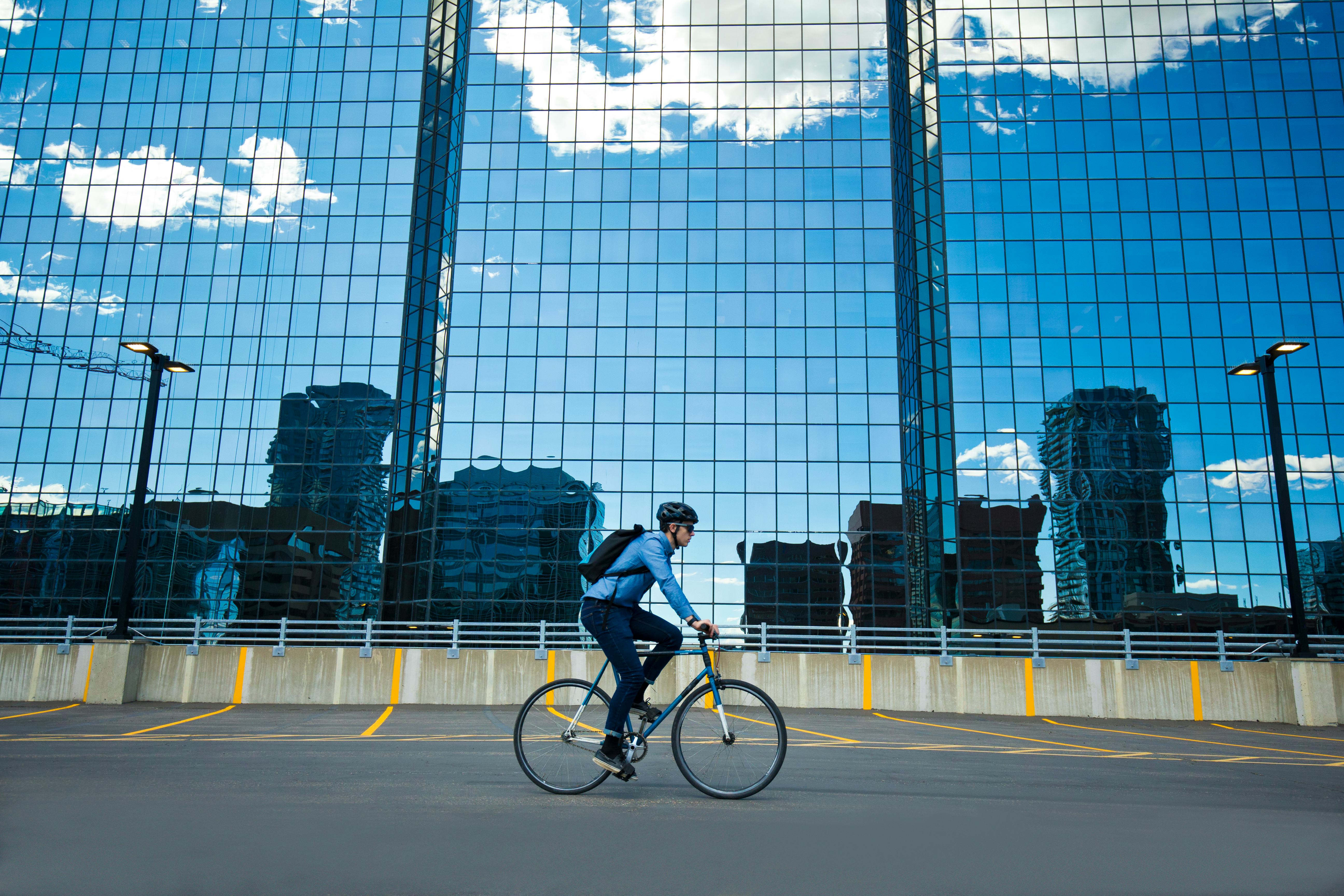 A male bicycle commuter rides his bike through a parking lot on his way to work in a big city. He ri...
