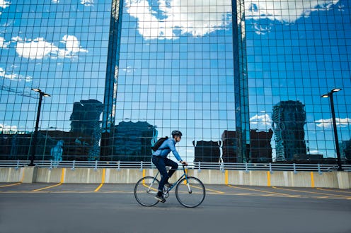 A male bicycle commuter rides his bike through a parking lot on his way to work in a big city. He ri...